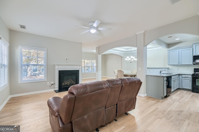 living room with ceiling fan with notable chandelier, light hardwood / wood-style floors, and sink