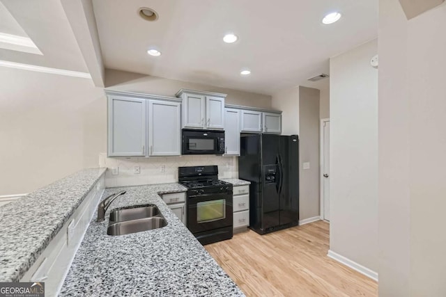 kitchen with light stone countertops, backsplash, sink, black appliances, and light hardwood / wood-style flooring