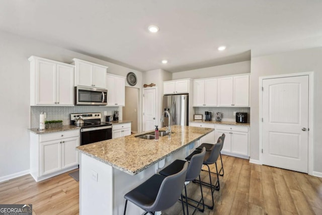 kitchen featuring a kitchen island with sink, white cabinets, a kitchen breakfast bar, sink, and appliances with stainless steel finishes