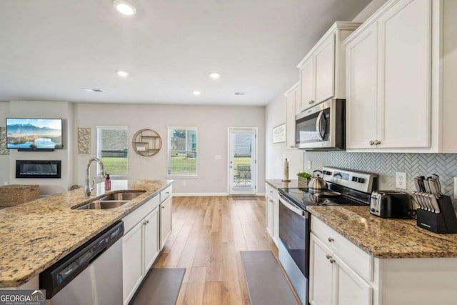 kitchen featuring light stone countertops, stainless steel appliances, sink, a center island with sink, and white cabinetry