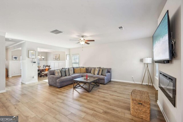 living room with ceiling fan with notable chandelier and light hardwood / wood-style flooring