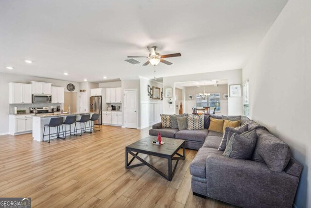 living room with light hardwood / wood-style floors and ceiling fan with notable chandelier