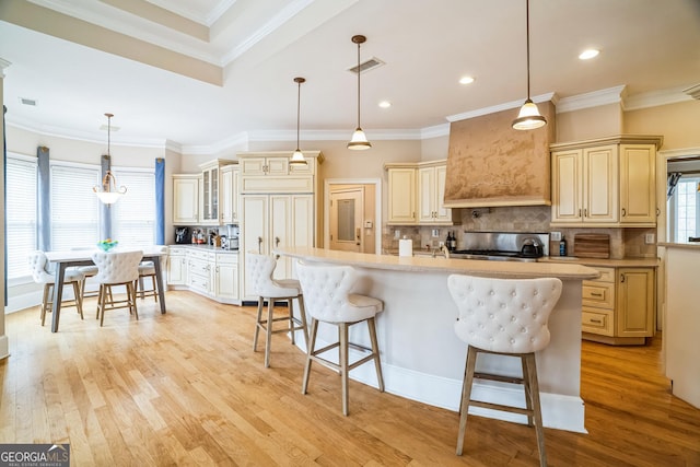 kitchen featuring a breakfast bar, tasteful backsplash, hanging light fixtures, a kitchen island with sink, and light wood-type flooring