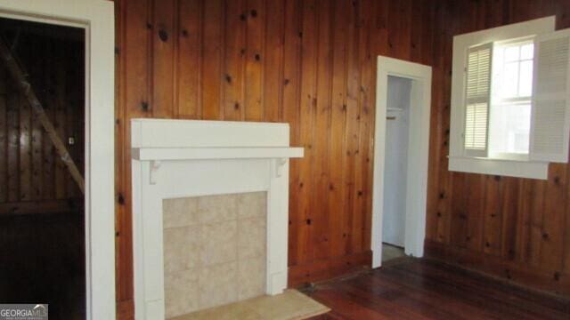 unfurnished living room with a tiled fireplace, wood walls, and dark wood-type flooring