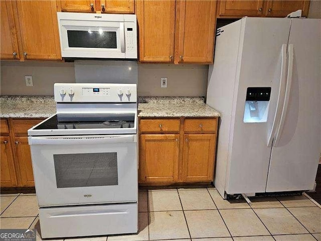 kitchen with light stone countertops, light tile patterned flooring, and white appliances