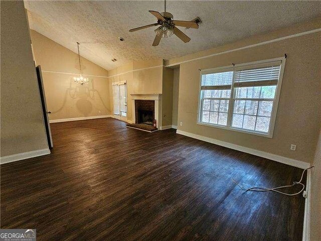 unfurnished living room featuring dark wood-type flooring, a textured ceiling, vaulted ceiling, a fireplace, and ceiling fan with notable chandelier