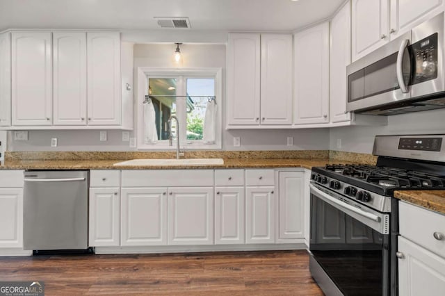 kitchen with appliances with stainless steel finishes, sink, dark stone countertops, white cabinets, and dark hardwood / wood-style floors