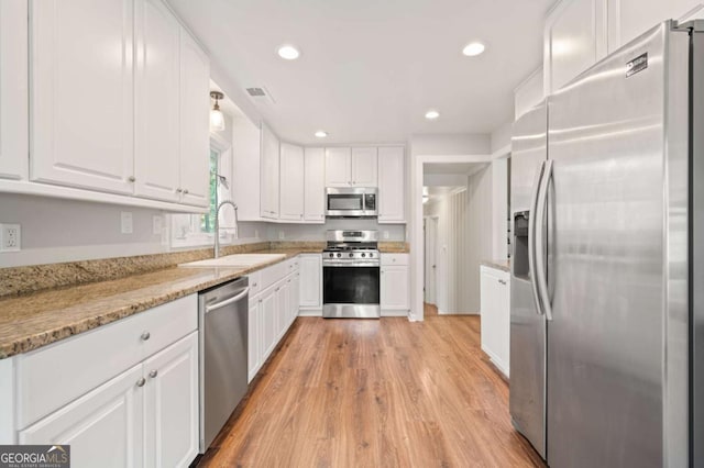 kitchen with light stone countertops, white cabinetry, sink, and stainless steel appliances