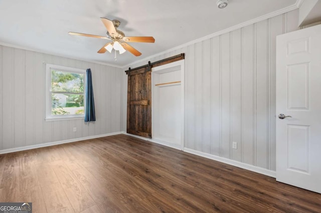 unfurnished bedroom with a barn door, ceiling fan, dark hardwood / wood-style floors, and ornamental molding