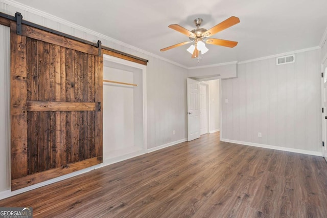 unfurnished bedroom with a barn door, ceiling fan, dark wood-type flooring, and ornamental molding