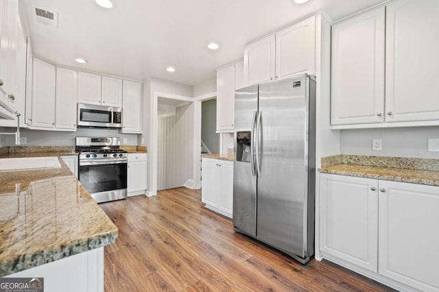 kitchen featuring appliances with stainless steel finishes, light stone counters, sink, wood-type flooring, and white cabinets