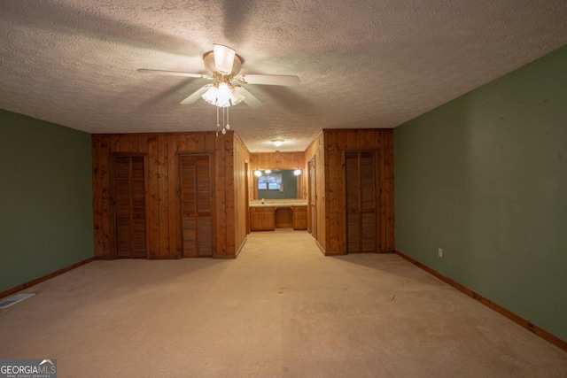 empty room featuring ceiling fan, wood walls, light colored carpet, and a textured ceiling