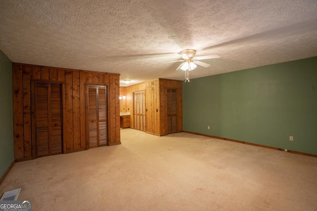 unfurnished bedroom featuring a textured ceiling, light colored carpet, ceiling fan, and wooden walls