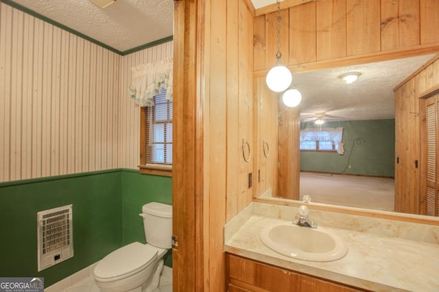 bathroom featuring heating unit, a textured ceiling, toilet, wooden walls, and vanity