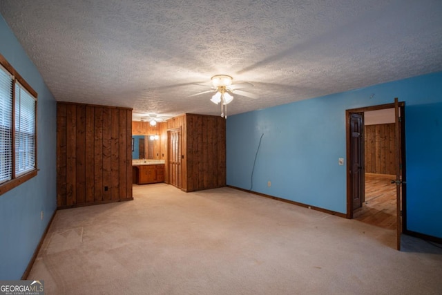 carpeted empty room with wooden walls, ceiling fan, and a textured ceiling