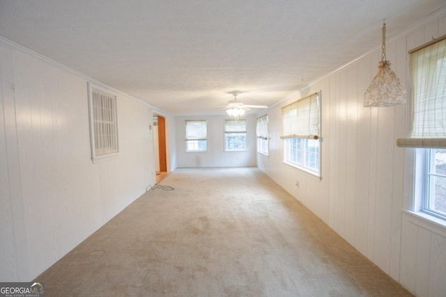 carpeted spare room with ceiling fan, wood walls, and crown molding