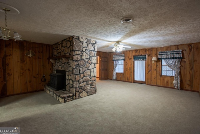 unfurnished living room featuring wood walls, a fireplace, light colored carpet, and ceiling fan with notable chandelier