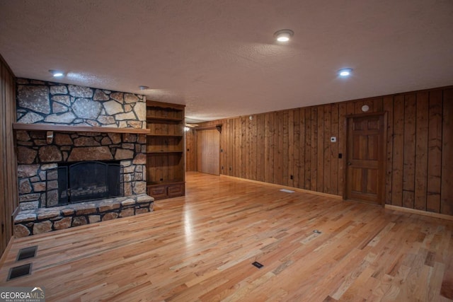 unfurnished living room featuring wooden walls, a fireplace, light hardwood / wood-style floors, and a textured ceiling