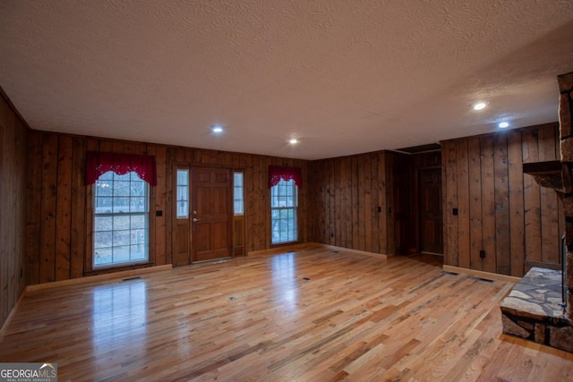 entryway with light wood-type flooring, a textured ceiling, and wooden walls