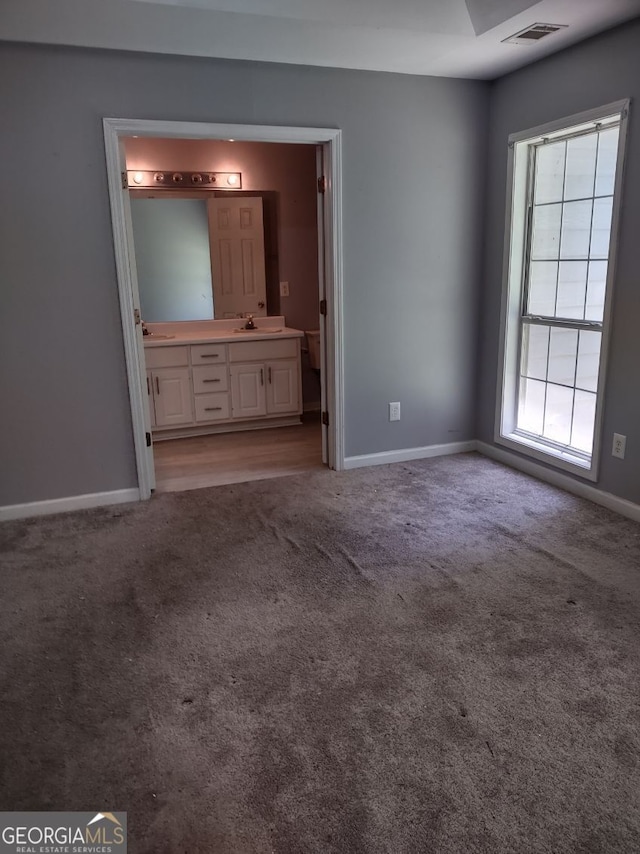 unfurnished bedroom featuring light carpet, ensuite bathroom, and sink