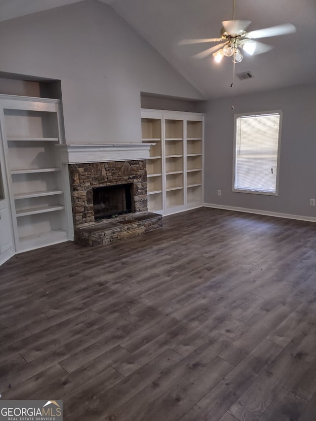 unfurnished living room with built in shelves, vaulted ceiling, ceiling fan, dark hardwood / wood-style floors, and a stone fireplace