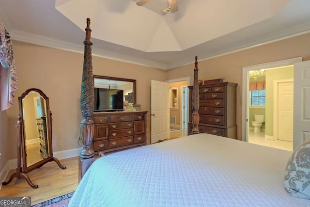 bedroom featuring ensuite bath, ornamental molding, a tray ceiling, ceiling fan, and light hardwood / wood-style flooring