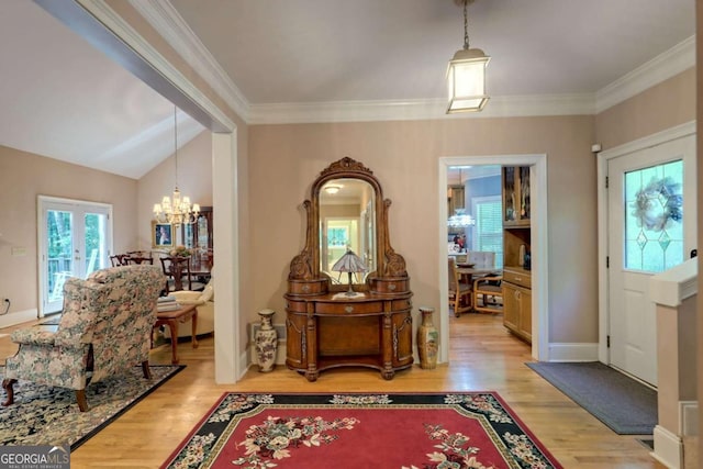 entryway featuring lofted ceiling, light wood-type flooring, ornamental molding, and an inviting chandelier