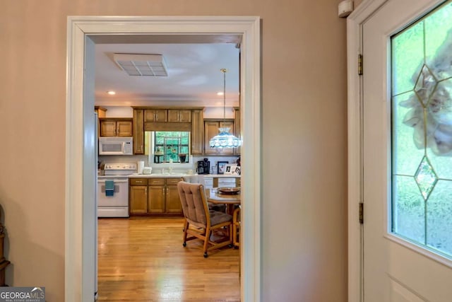 kitchen with white appliances, light hardwood / wood-style flooring, plenty of natural light, and hanging light fixtures