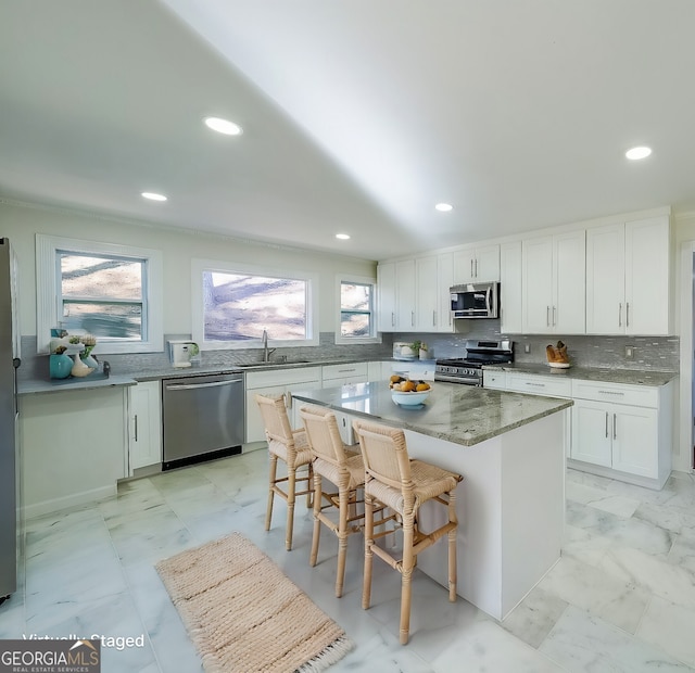 kitchen with tasteful backsplash, a kitchen island, a breakfast bar area, stainless steel appliances, and white cabinets