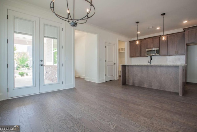 kitchen featuring french doors, tasteful backsplash, crown molding, hanging light fixtures, and an island with sink