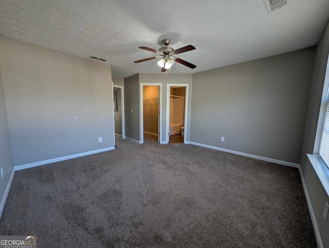 unfurnished bedroom featuring dark carpet, ceiling fan, a spacious closet, a textured ceiling, and a closet