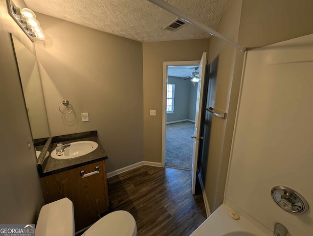 bathroom with ceiling fan, wood-type flooring, a textured ceiling, toilet, and vanity