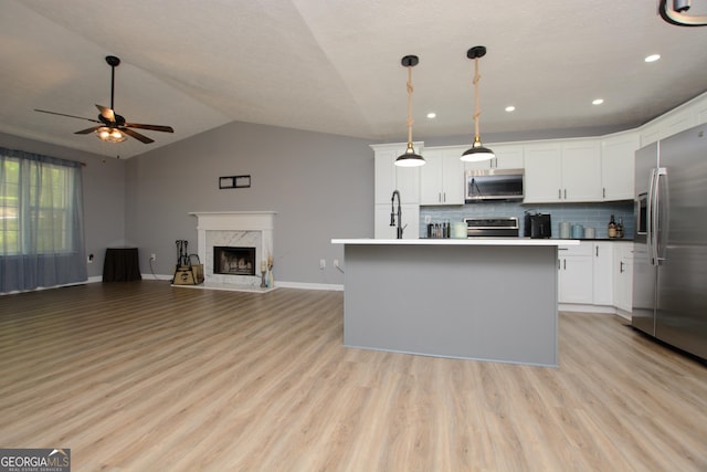 kitchen with tasteful backsplash, an island with sink, lofted ceiling, white cabinets, and appliances with stainless steel finishes