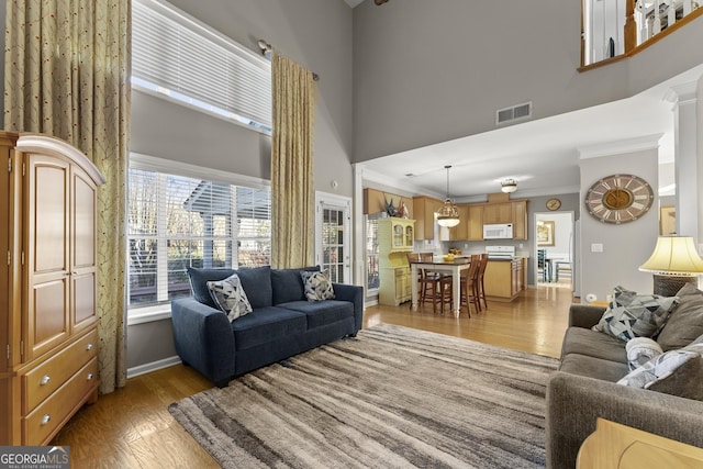 living room with a high ceiling, crown molding, and light wood-type flooring