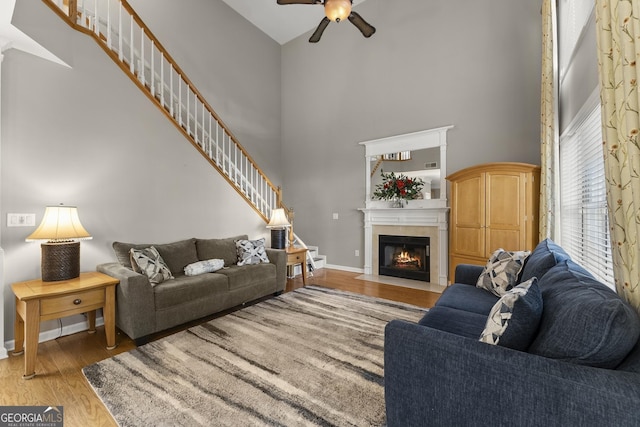 living room featuring ceiling fan, a towering ceiling, and light hardwood / wood-style floors