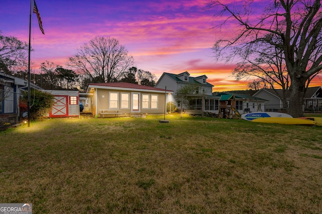 back house at dusk featuring a shed and a lawn