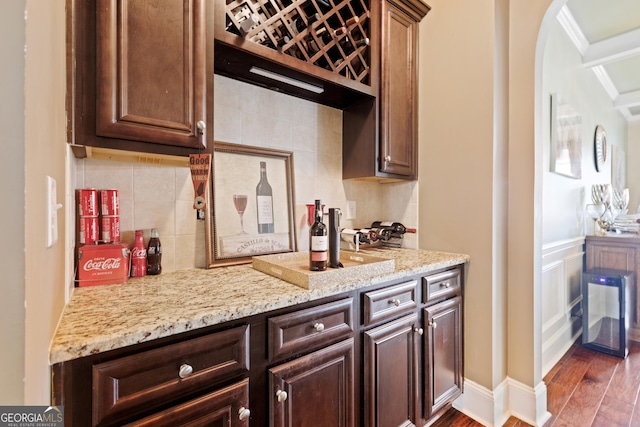 kitchen featuring dark wood-type flooring, light stone countertops, ornamental molding, tasteful backsplash, and dark brown cabinets