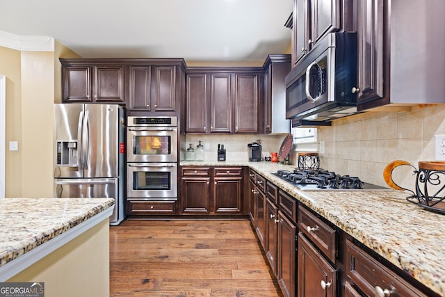 kitchen with decorative backsplash, light stone countertops, dark brown cabinets, stainless steel appliances, and light hardwood / wood-style flooring