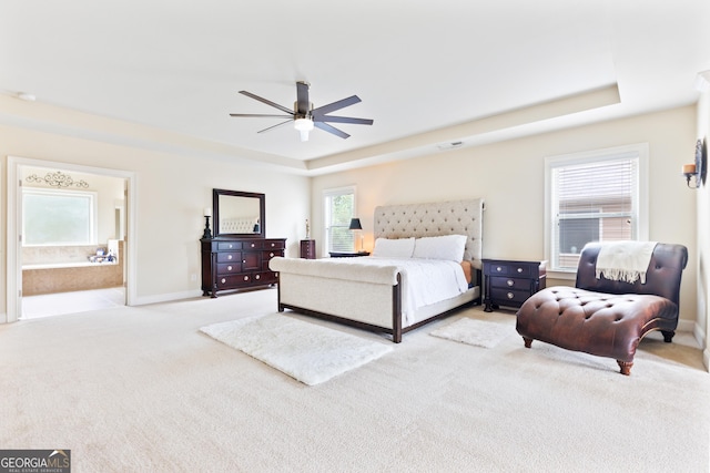 bedroom featuring ceiling fan, light colored carpet, ensuite bathroom, and a tray ceiling