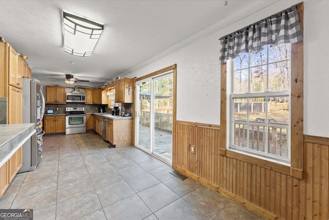 kitchen with appliances with stainless steel finishes, ornamental molding, ceiling fan, sink, and light tile patterned floors