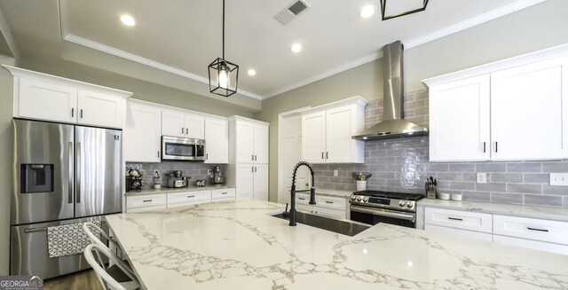 kitchen featuring wall chimney exhaust hood, stainless steel appliances, backsplash, decorative light fixtures, and white cabinets