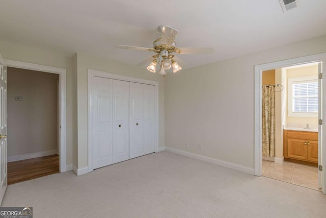 unfurnished bedroom with connected bathroom, ceiling fan, a closet, and light carpet