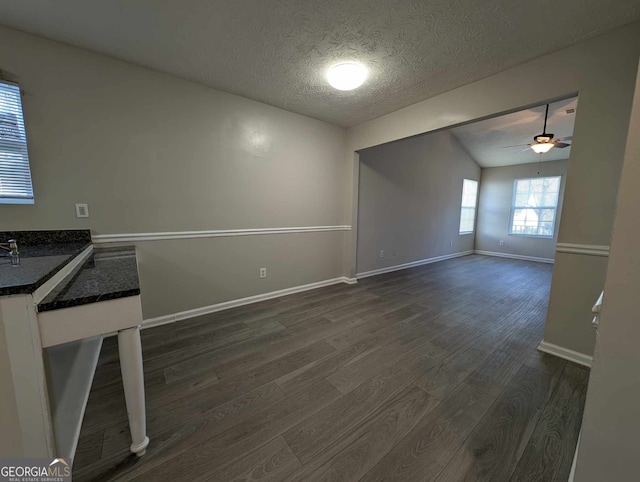 unfurnished living room with vaulted ceiling, ceiling fan, dark hardwood / wood-style flooring, and a textured ceiling