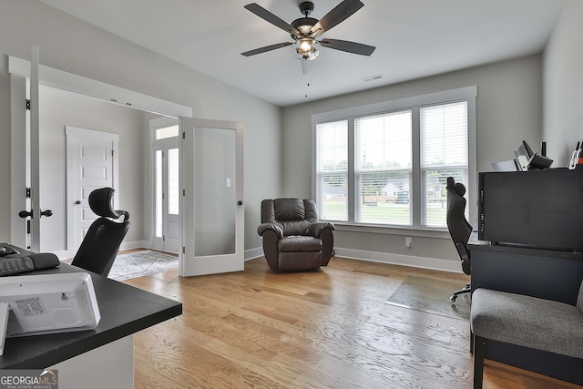 home office with a wealth of natural light, light hardwood / wood-style flooring, ceiling fan, and french doors