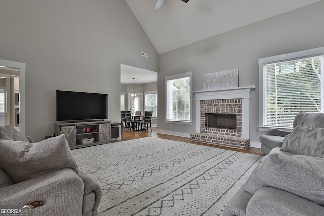 living room featuring ceiling fan with notable chandelier, a healthy amount of sunlight, high vaulted ceiling, and a brick fireplace