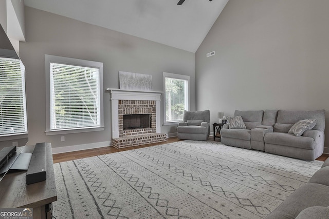 living room with wood-type flooring, high vaulted ceiling, a brick fireplace, and ceiling fan