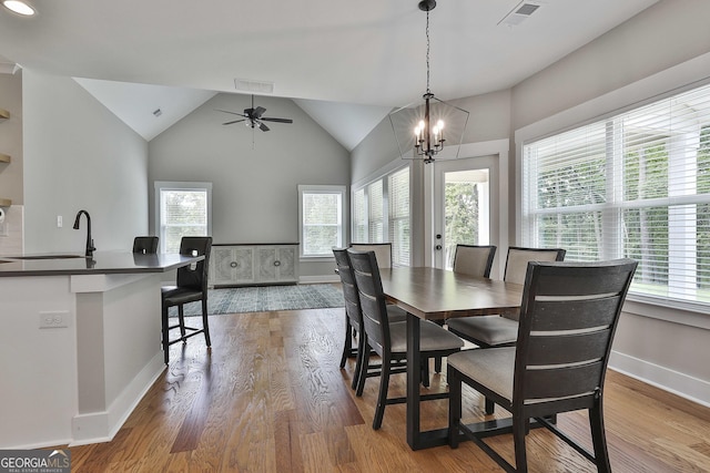 dining space with wood-type flooring, ceiling fan with notable chandelier, lofted ceiling, and sink