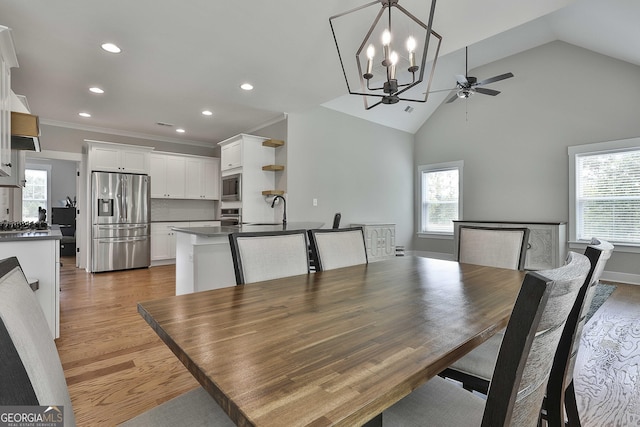 dining area with high vaulted ceiling, ceiling fan with notable chandelier, crown molding, sink, and light wood-type flooring