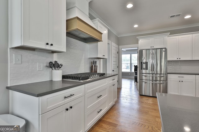 kitchen featuring white cabinetry, premium range hood, backsplash, crown molding, and appliances with stainless steel finishes