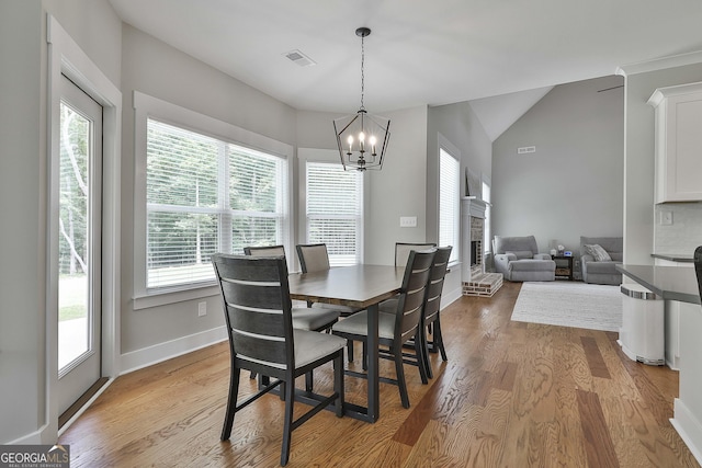 dining room featuring a fireplace, vaulted ceiling, a chandelier, and light hardwood / wood-style flooring